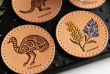 Set of four leather coasters with Australian designs on a black textured surface.